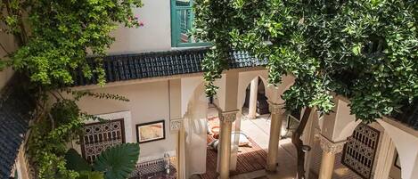 An indoor courtyard with a tiled roof, arches, and a large tree providing shade.