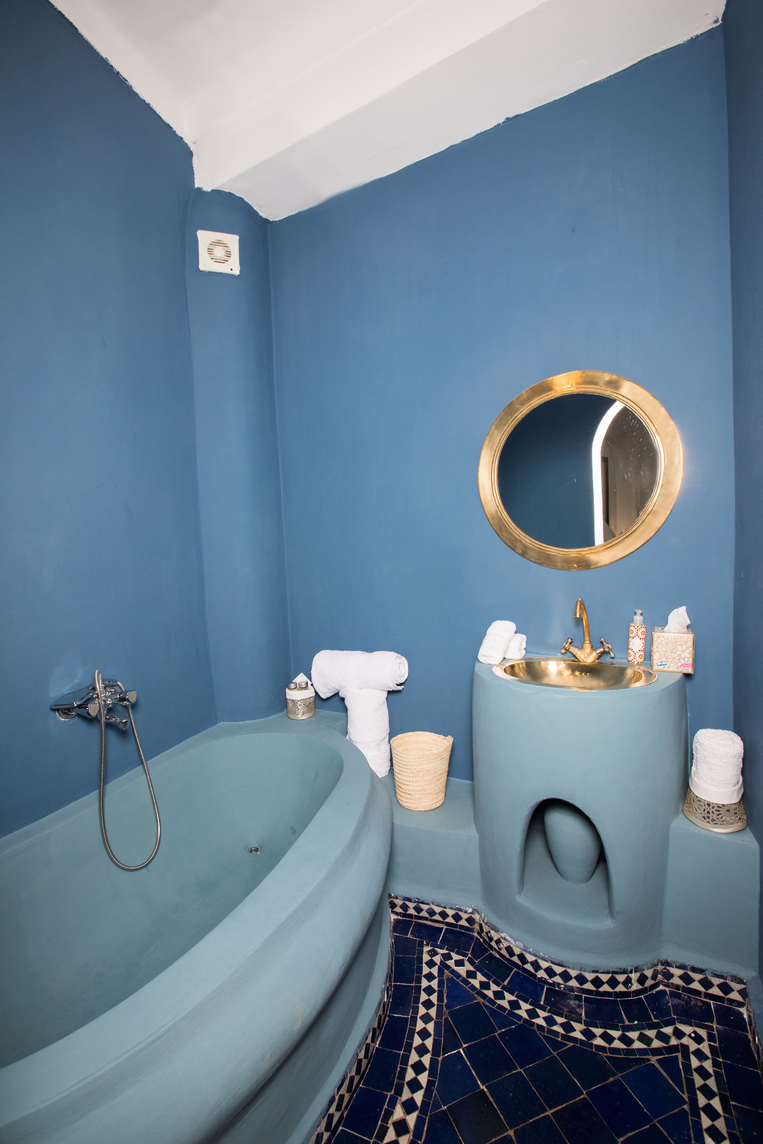 A bathroom with a blue sink, a round mirror, a bathtub, and a patterned floor.