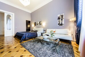 A modern living room with a sofa, a coffee table, and a bed with a blue bedspread. - Matei Corvin Apartments (Cluj-Napoca)