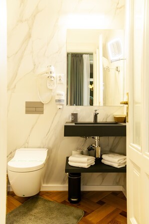 A bathroom with a marble wall, a black sink, a toilet, a mirror, and a hairdryer on the wall. - Matei Corvin Apartments (Cluj-Napoca)