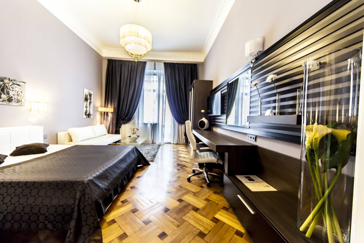 A hotel room with a bed, a desk, a chair, a television, and a vase with flowers.