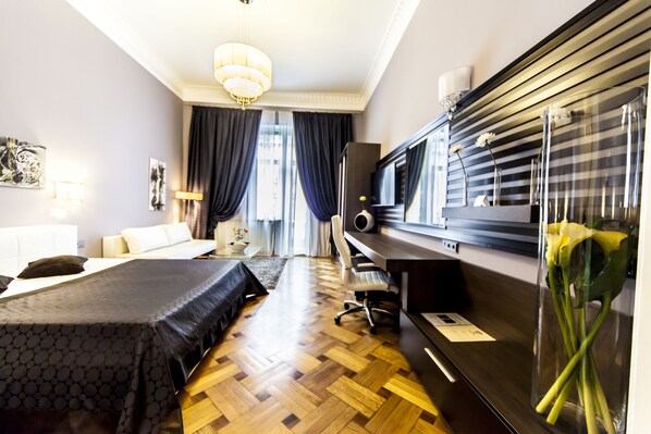 A hotel room with a bed, a desk, a chair, a television, and a vase with flowers. - Matei Corvin Apartments (Cluj-Napoca)
