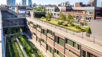 A modern building with a rooftop garden, large windows, and a cityscape in the background.
