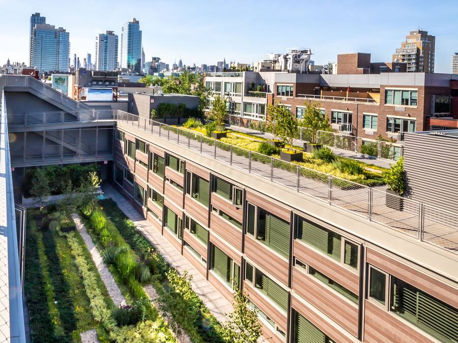 A modern building with a rooftop garden, large windows, and a cityscape in the background.
