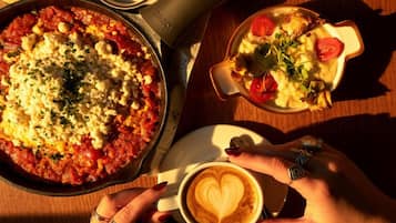 A table with a variety of dishes including a pizza, a bowl of salad, and a bowl of soup. There is also a cup of coffee with a heart-shaped latte art.