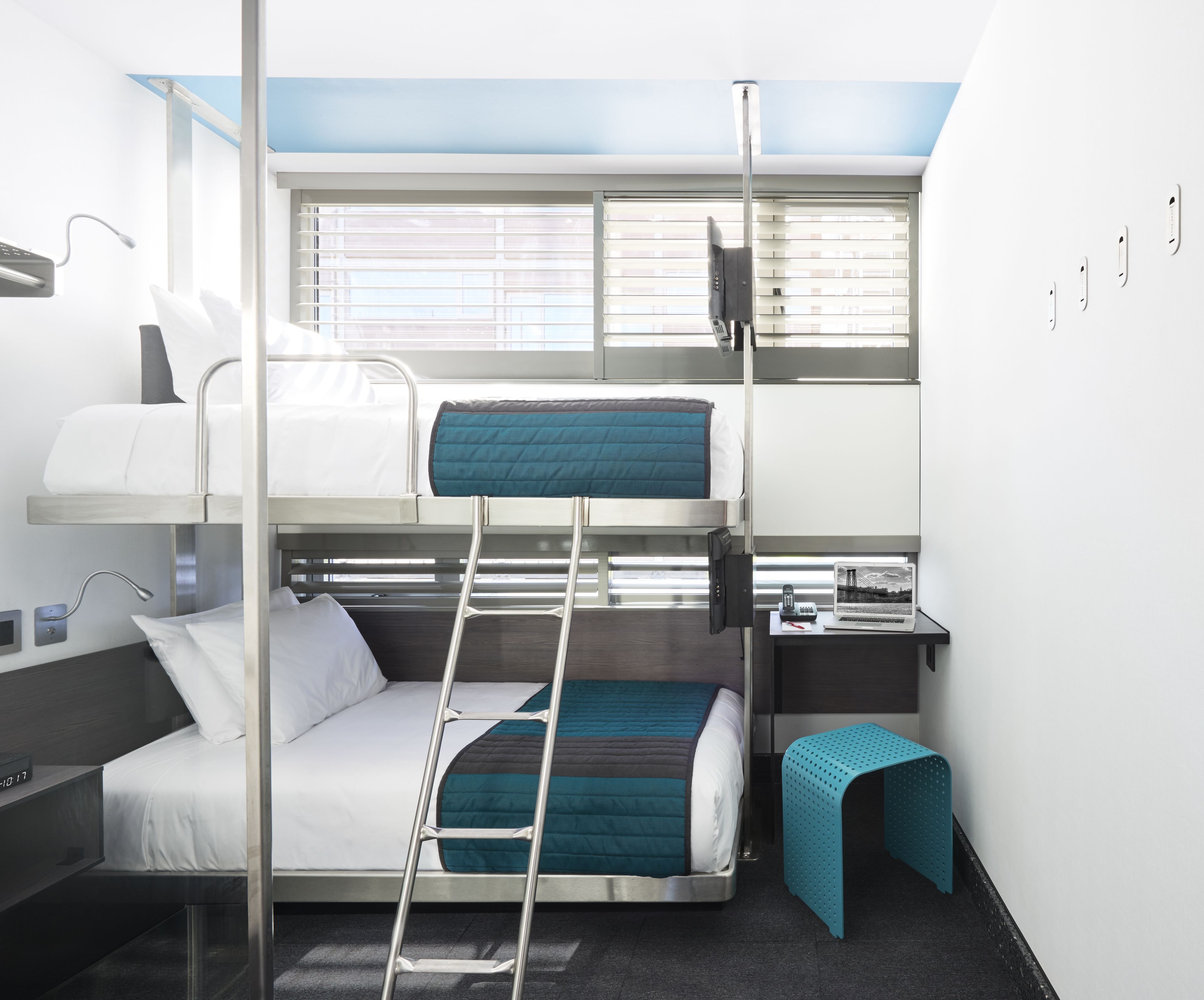 A bunk bed room with a desk, a laptop, and a window with blinds.