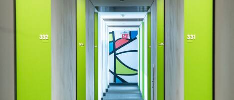 A hallway with green walls and carpeted floors, leading to an exit with a red and blue sign.