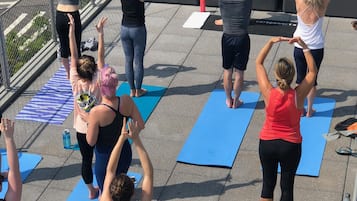 A group of people performing yoga on outdoor mats in an urban setting with brick walls and greenery in the background.