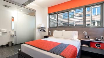 A hotel room with a bed, bedside table, and a window with blinds.