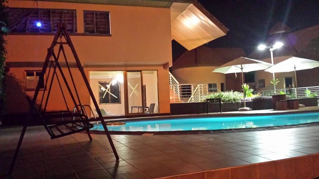 A swimming pool area with a swing chair, umbrellas, and a building with a staircase and glass doors.