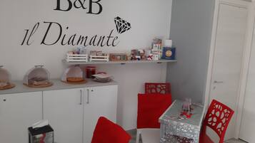 A dining area with a white table, red chairs, and a shelf above the table with various items.