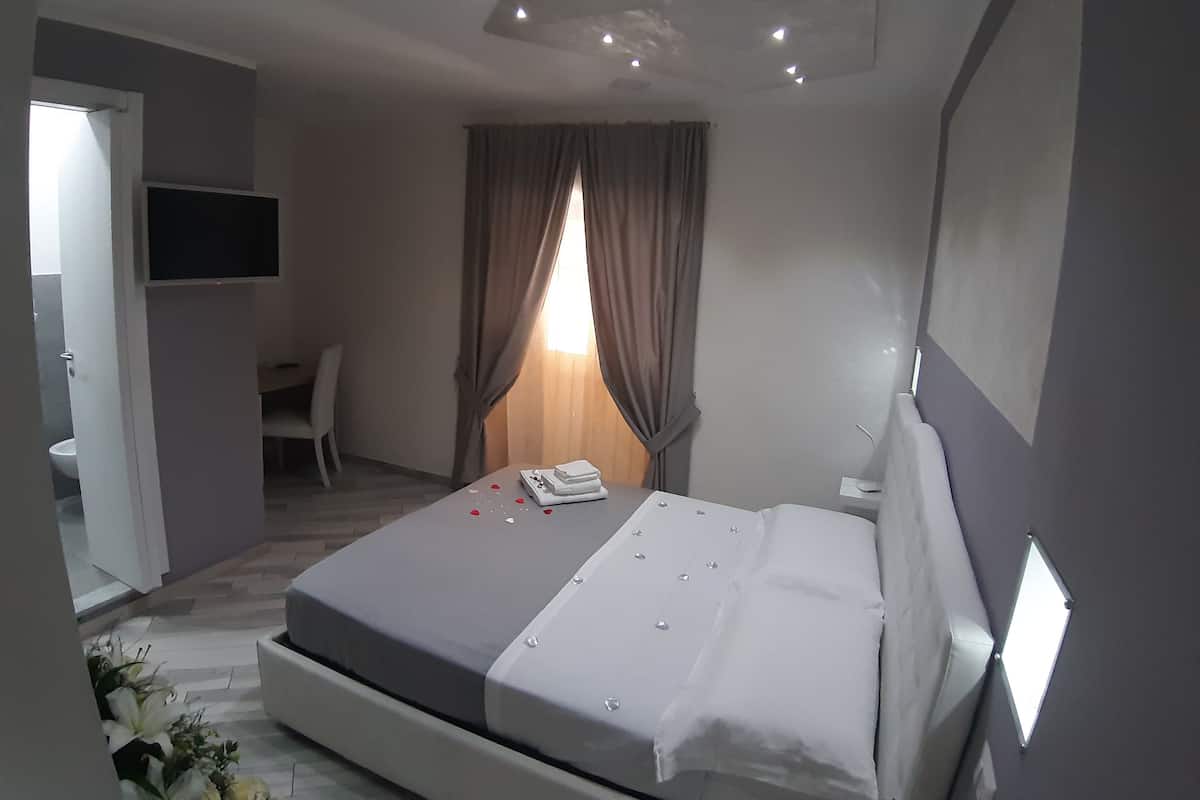 A modern hotel room with a bed, a desk, a chair, and a TV mounted on the wall.