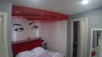 Een moderne slaapkamer met een rode hoofdbord, een bed met witte lakens en een muur met twee grote, opvallende ontwerpen.
