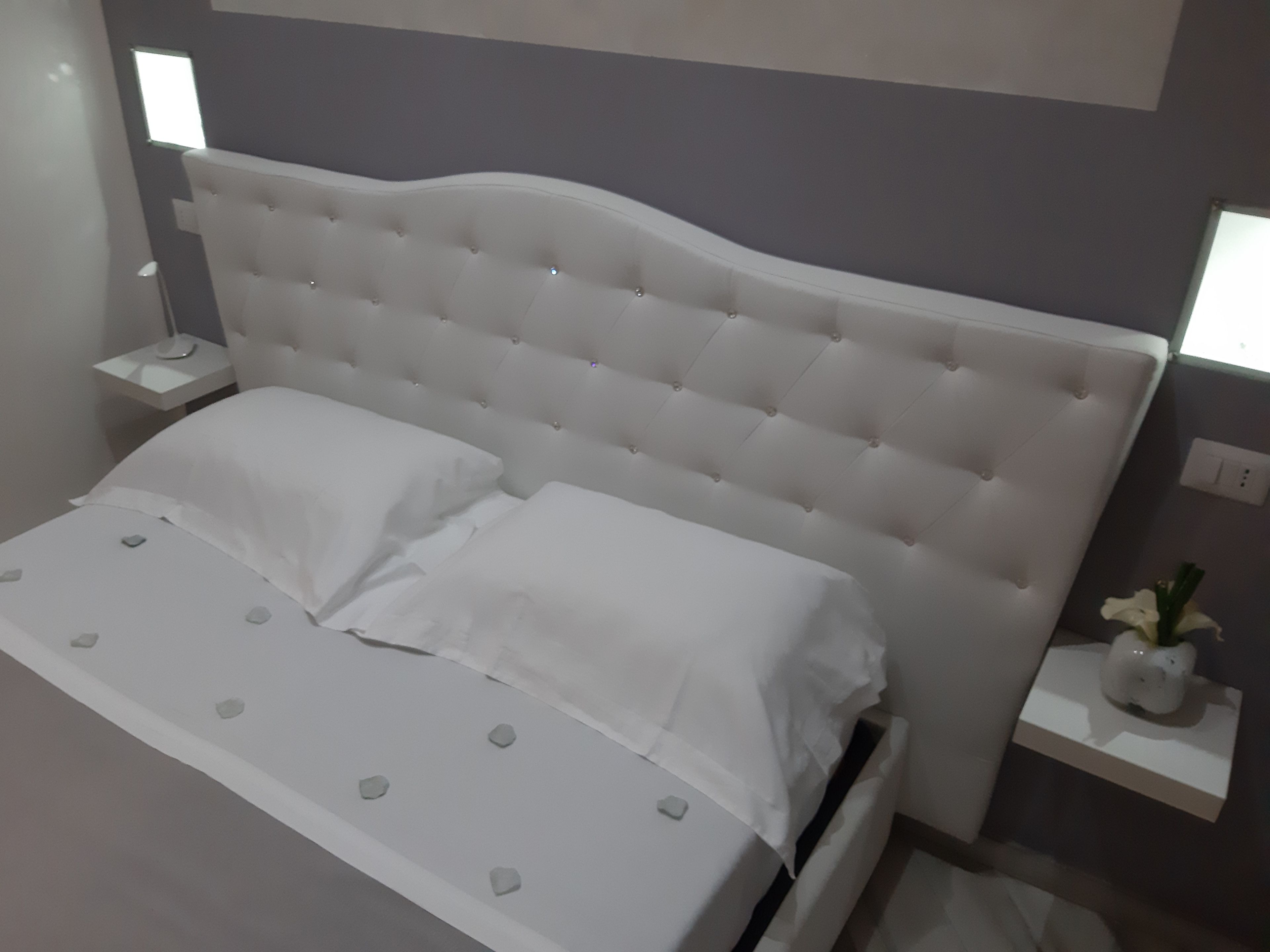 A modern bedroom with a tufted headboard, white bedding, and bedside tables with lamps.