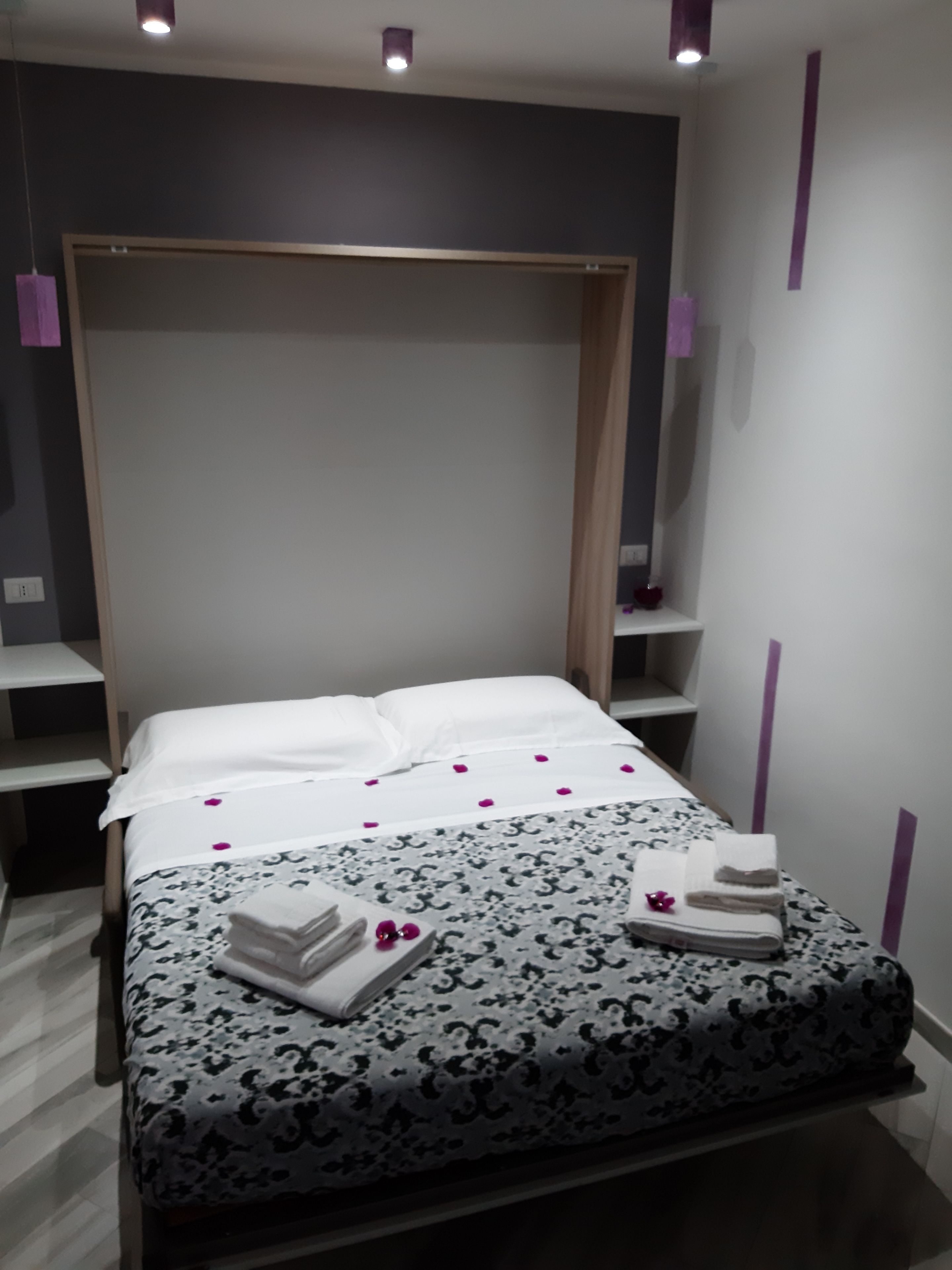 A modern bedroom with a large bed, a wooden headboard, and a bedside table with a lamp.