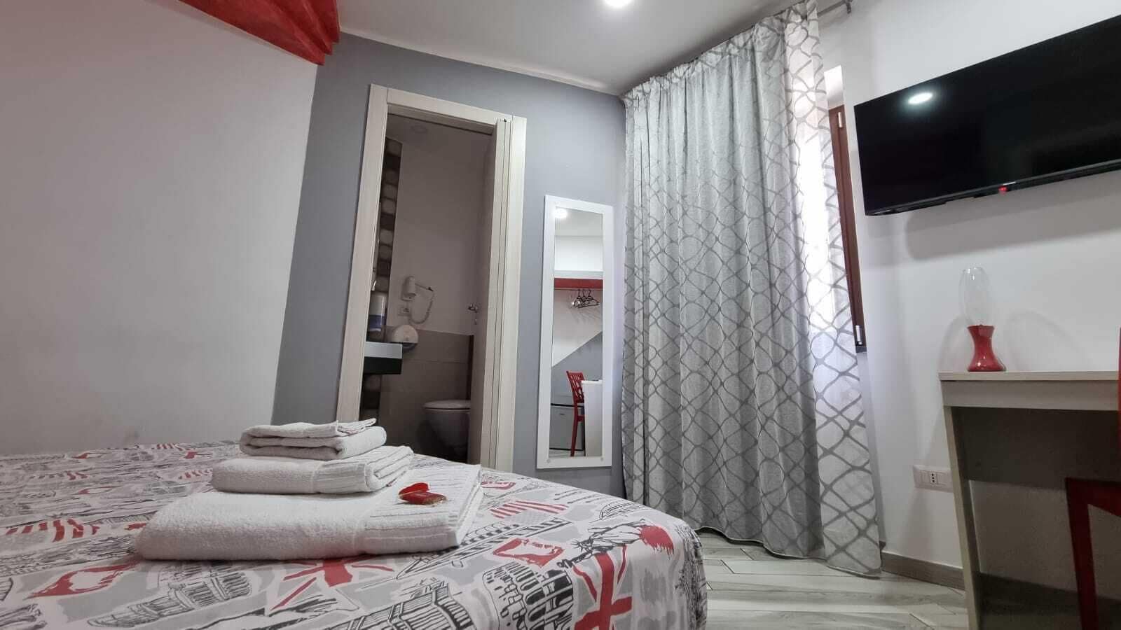 Une chambre à coucher avec un lit, une télévision, un bureau et une salle de bain visible à travers une porte ouverte.