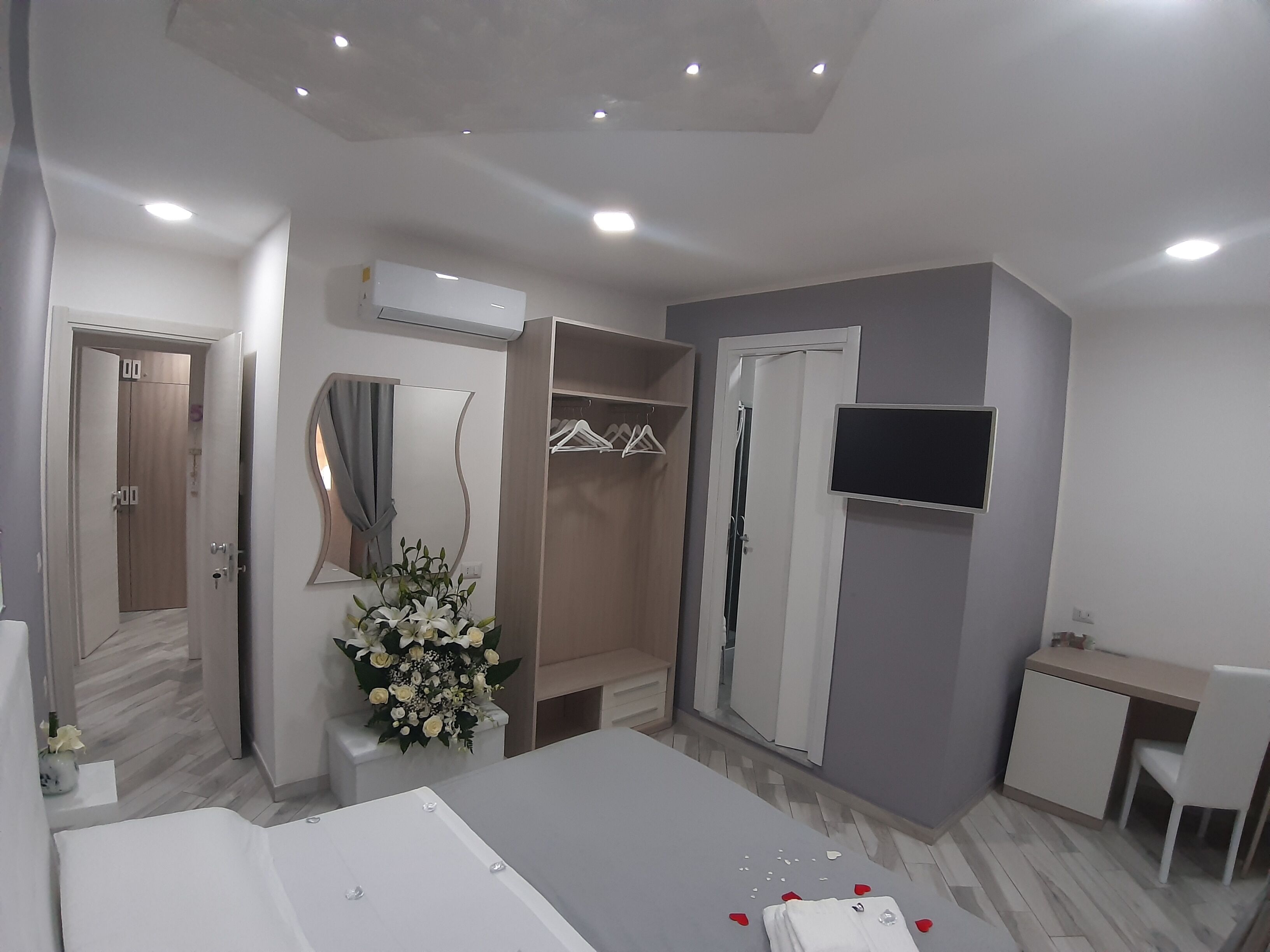 A modern bedroom with a bed, a desk, a TV, and a wardrobe.
