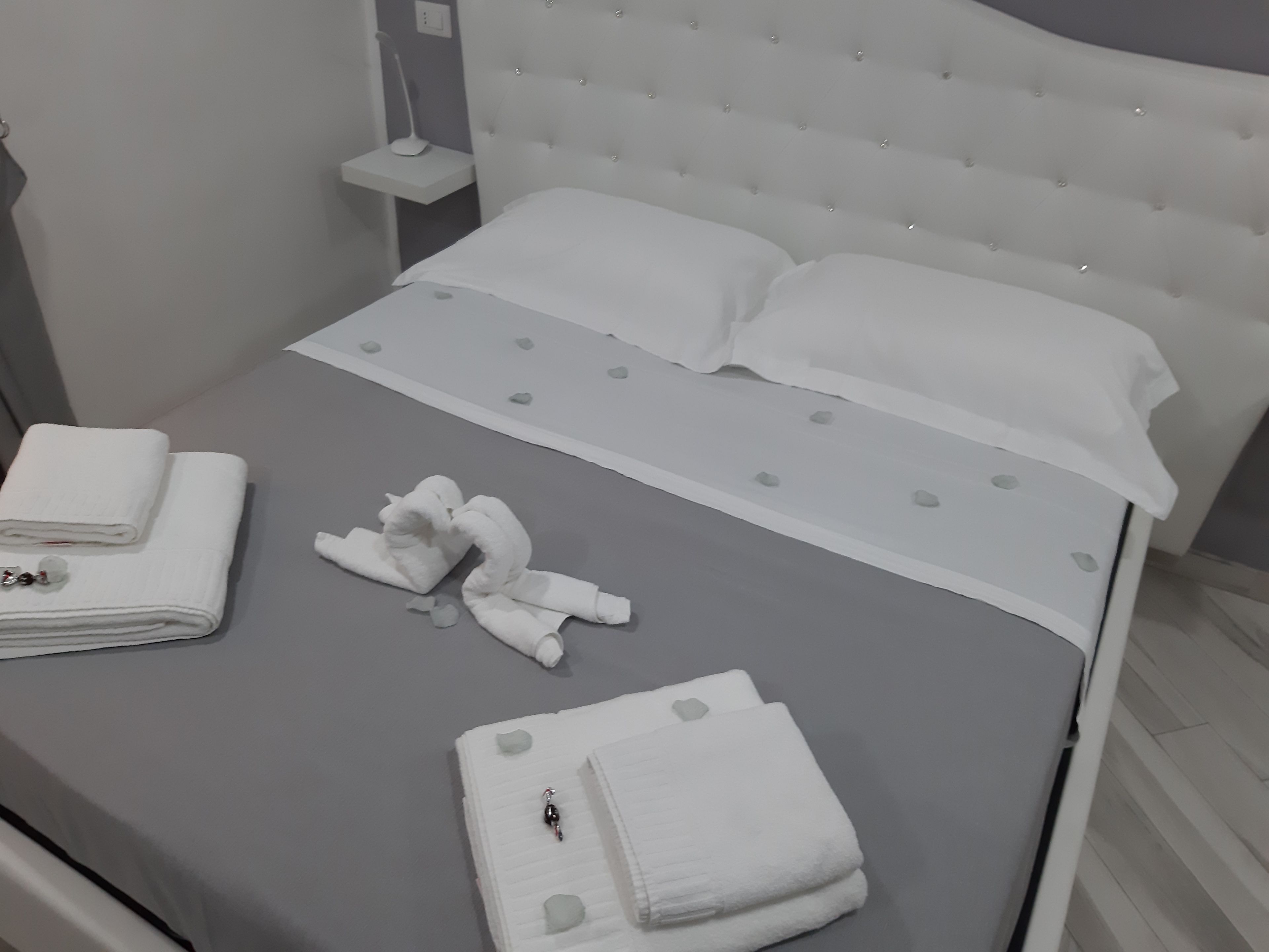 Una cama bien hecha con sábanas blancas, una mesita de noche con lámpara y un cabecero moderno.