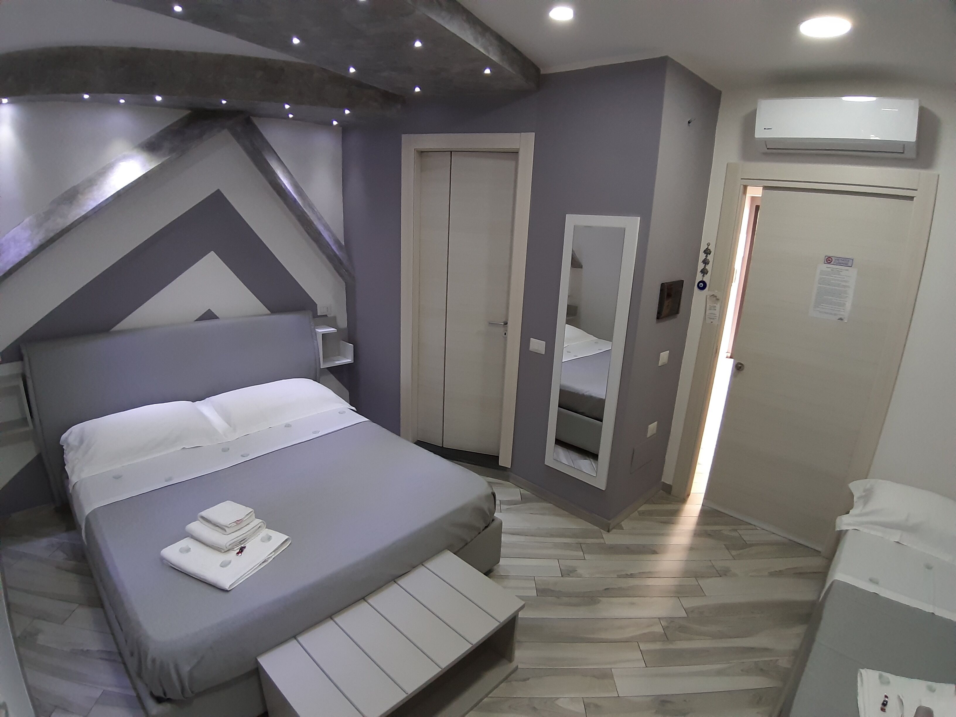 A bedroom with a bed, a built-in bench, a wardrobe, a mirror, and an air conditioning unit.
