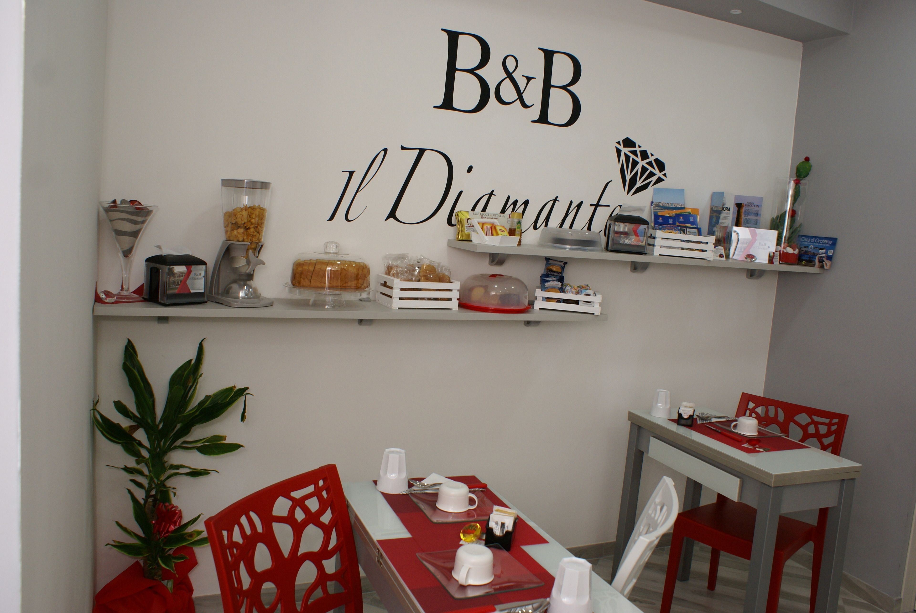 A dining area with a B&B sign, red chairs, white table, and various food items on shelves.