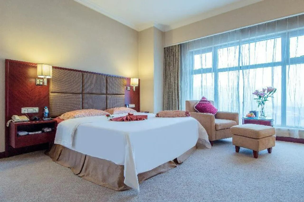 A hotel room with a large bed, a chair, a small table, and a window with curtains.