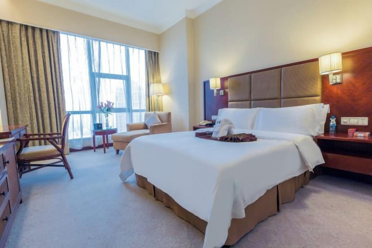 Una habitación de hotel con una cama grande, un escritorio, una silla y un ventanal con cortinas.