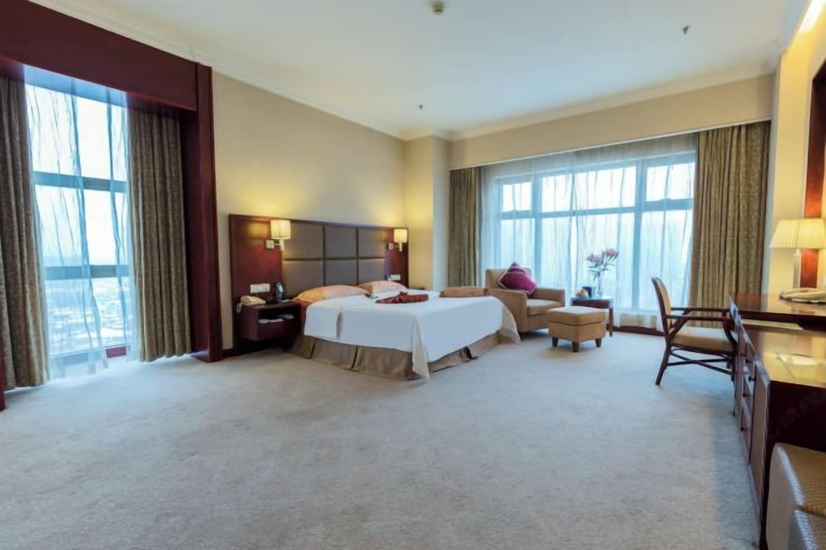 Habitación de hotel con una cama grande, un escritorio, una silla y vistas al exterior a través de las ventanas.