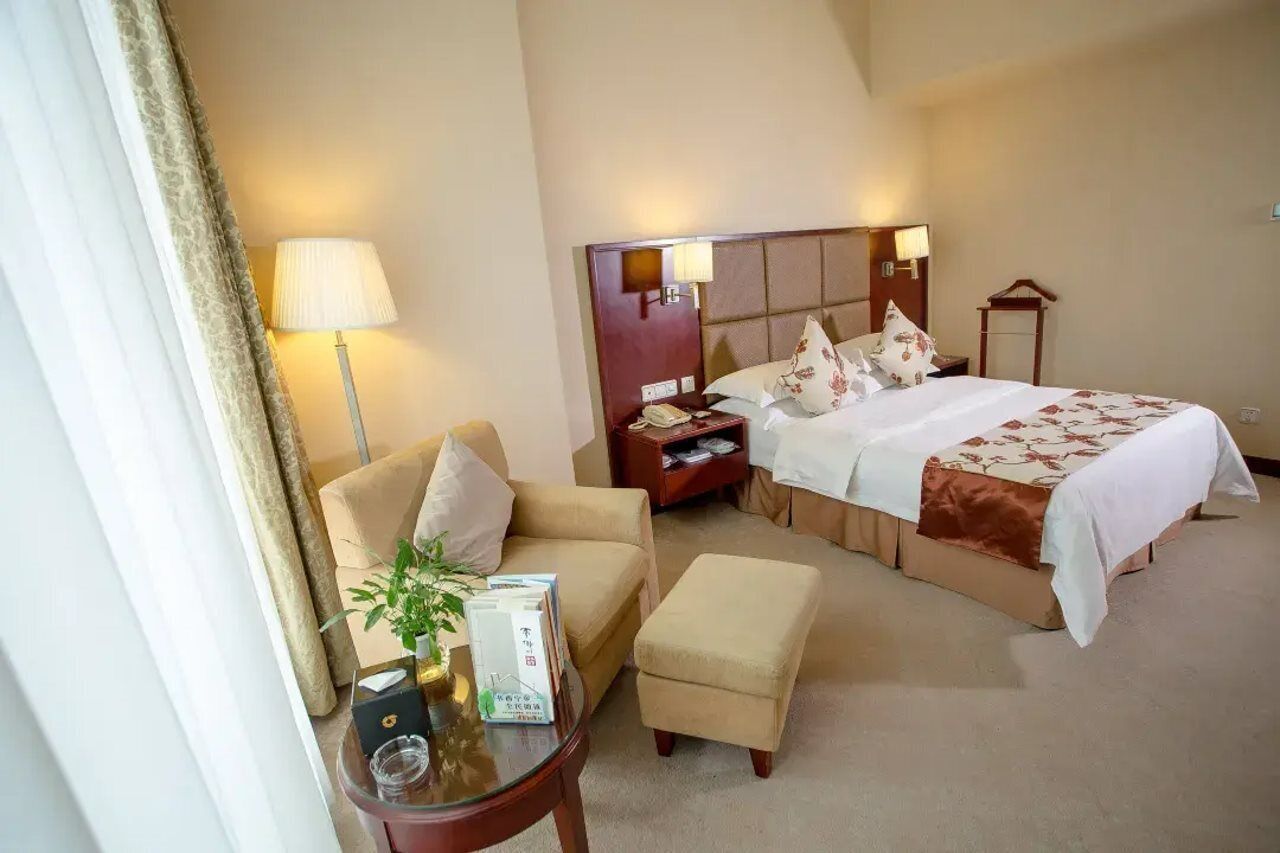 A hotel room with a large bed, a sofa, a small table with a lamp, and a nightstand with a lamp.