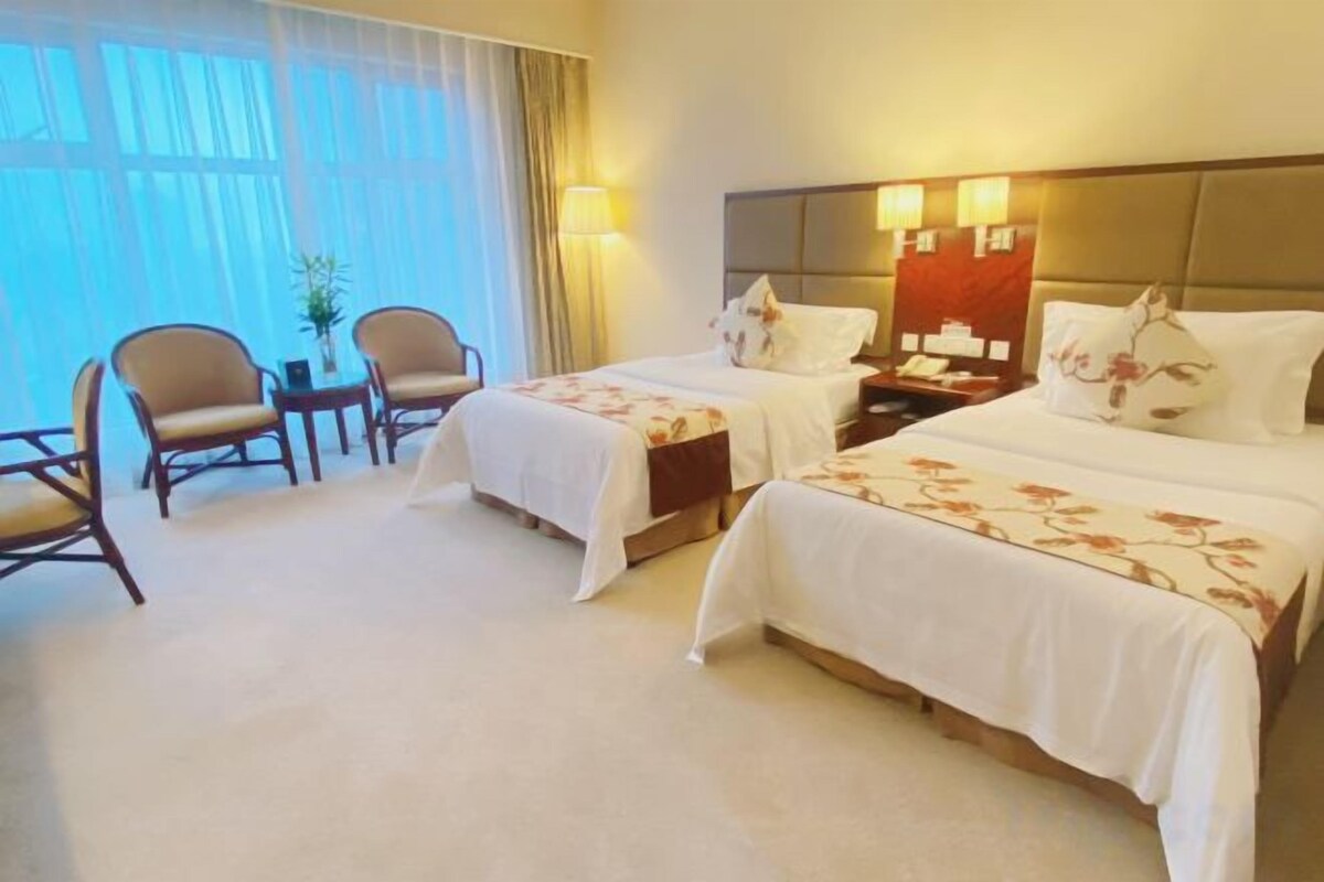 A hotel room with two beds, a desk, chairs, and a large window.