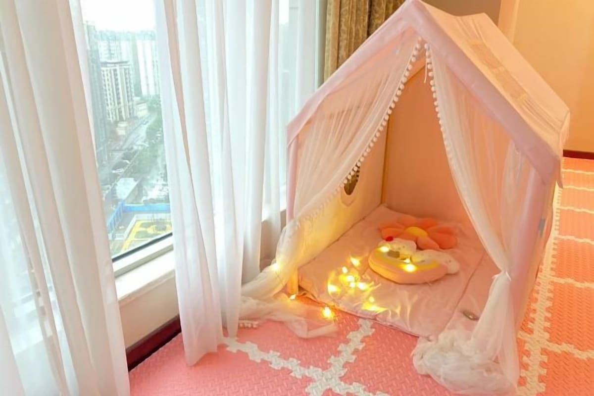 Una habitación acogedora con una cama a dosel, una alfombra rosa y vistas a un paisaje urbano a través de cortinas de encaje.