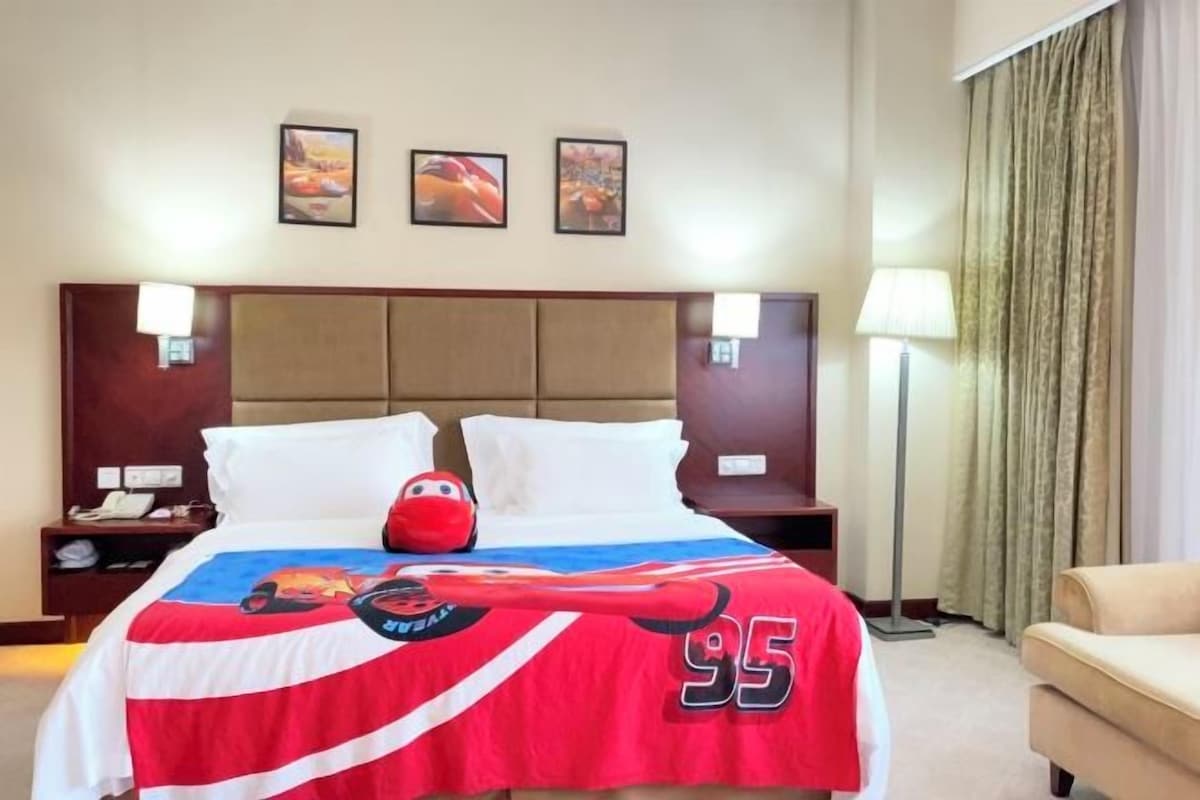 Una habitación de hotel con una cama grande, cabecera, dos mesitas de noche, una lámpara, un sofá y cortinas.