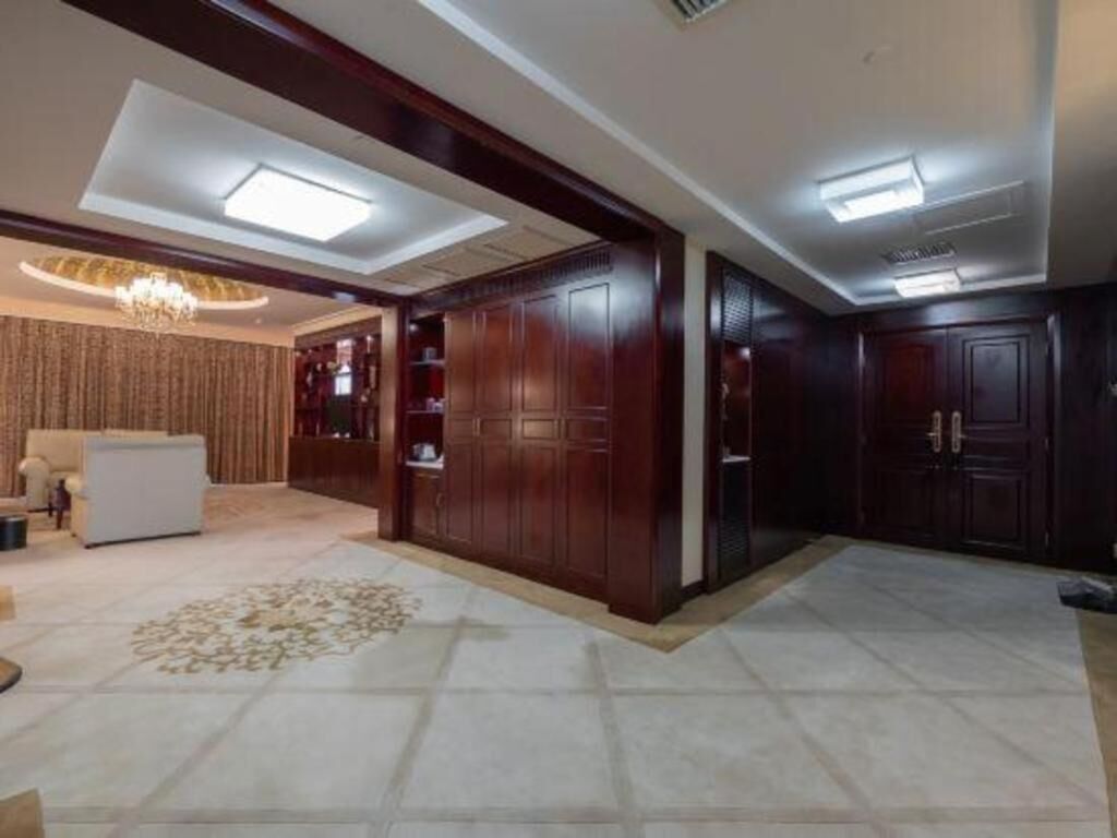 A spacious living area with a sofa, a coffee table, and a patterned rug. There are wooden cabinets and a chandelier.