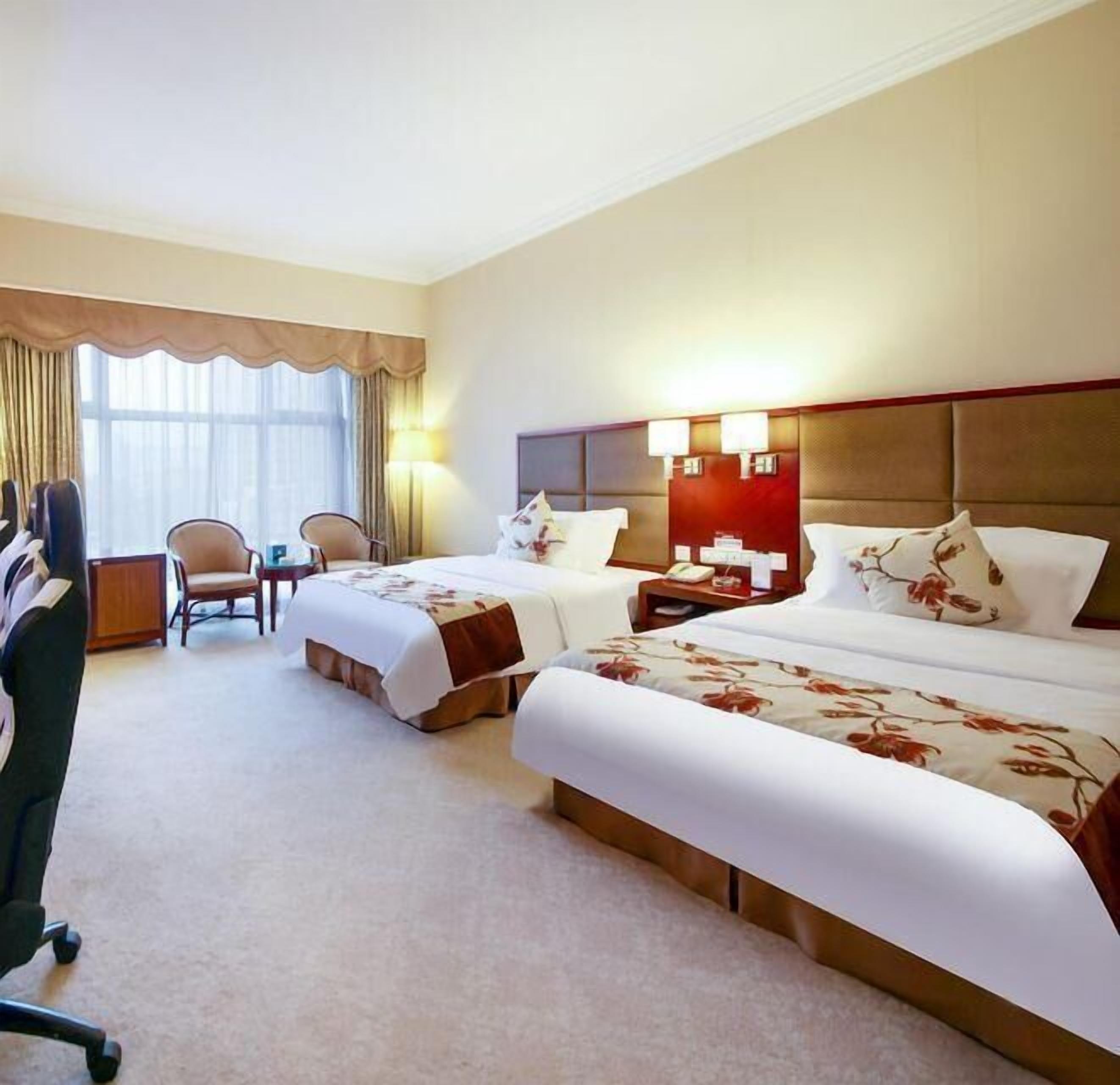 Une chambre d’hôtel avec deux lits, un bureau, une chaise et une grande fenêtre avec des rideaux.