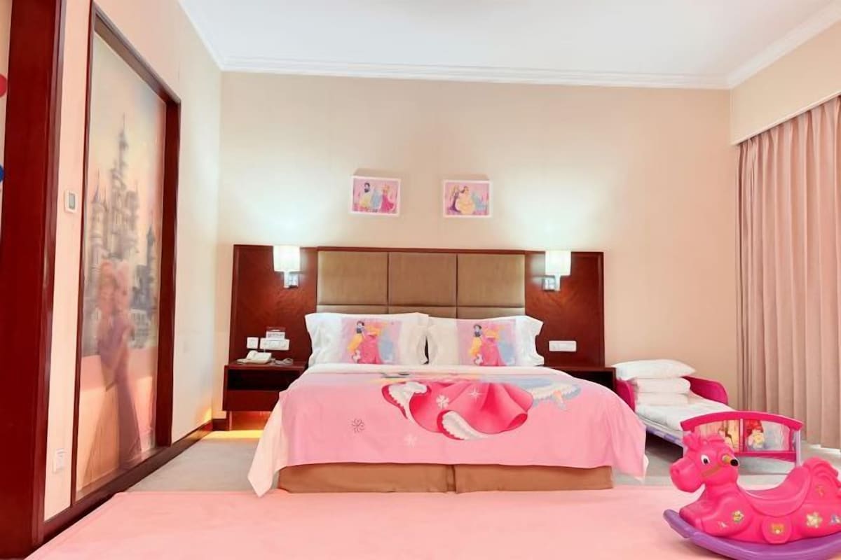 Una habitación de hotel con una cama grande, una mesita de noche, un aparador y un caballito de juguete rosa.