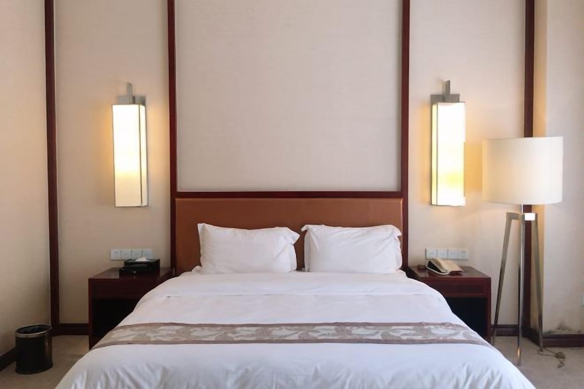 Habitación de hotel con una cama grande, dos mesitas de noche, una lámpara y un cesto de basura.