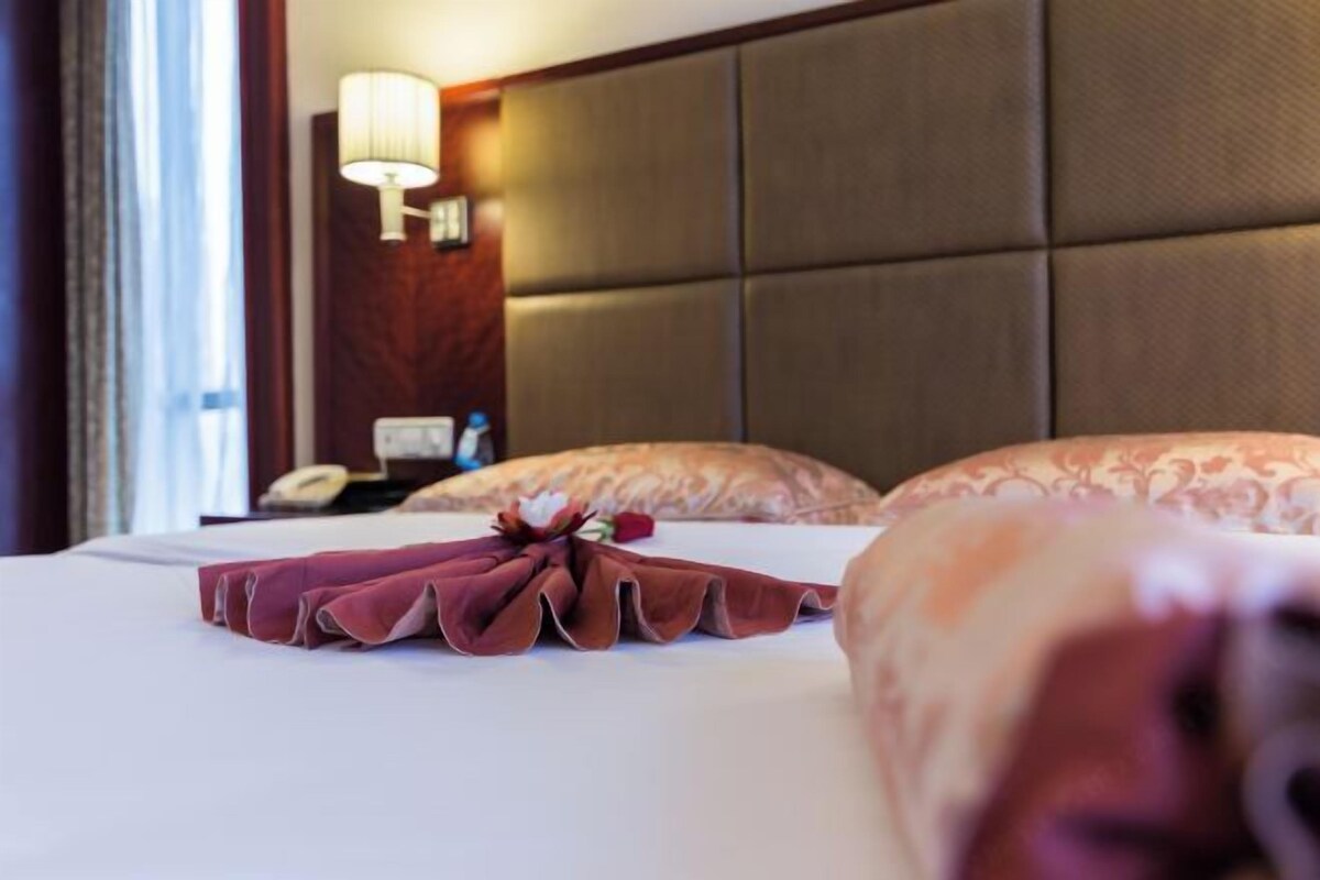 A hotel room with a neatly made bed, a headboard, and a bedside lamp.