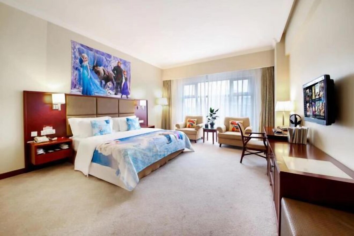 A hotel room with a large bed, a desk, a chair, a TV, and a window with curtains.