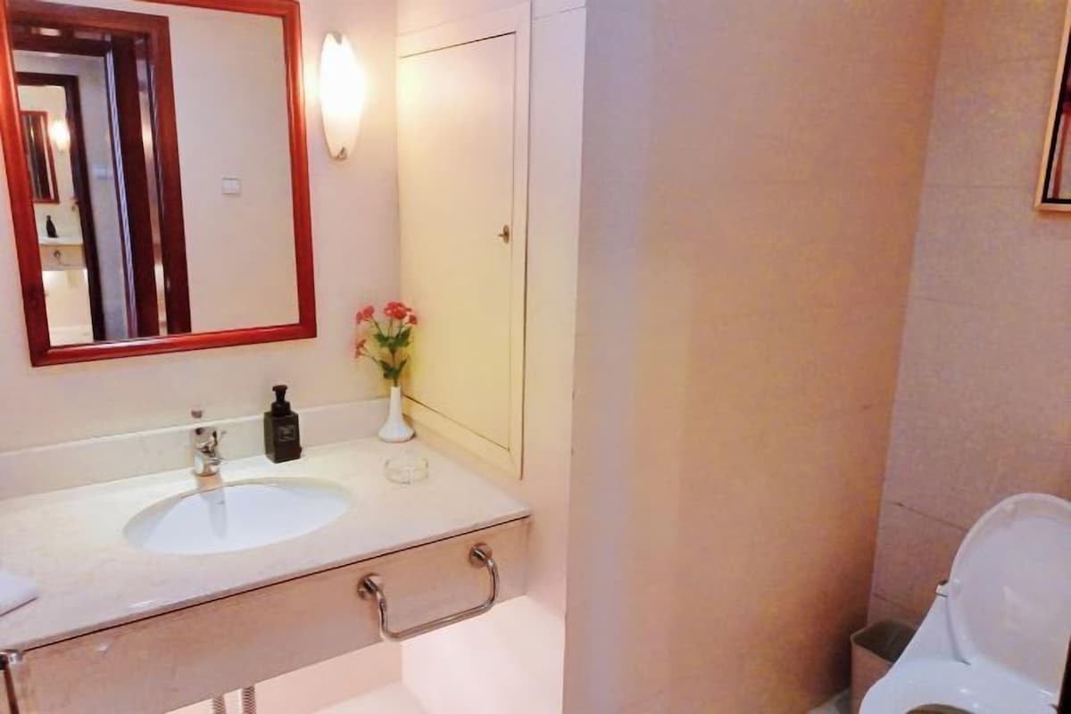 Un baño con dos lavamanos, un espejo, un jarrón con flores y un inodoro.