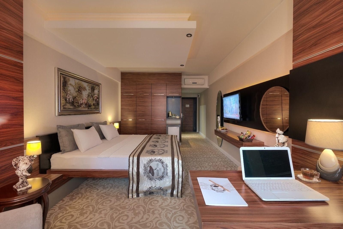Une chambre d’hôtel avec un lit, un bureau avec un ordinateur portable, une télévision, un miroir et un tableau au mur.