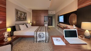 A hotel room with a bed, a desk with a laptop, a TV, a mirror, and a painting on the wall. - Madame Tadia Hotel (Eskisehir)