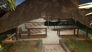 An outdoor dining area with a thatched roof, brick walls, and wooden tables and benches.