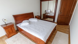 A neatly made bed with white linens, a wooden headboard, and a large mirror on the wall. - Cluj Lux Apartments Platinia (Cluj-Napoca)