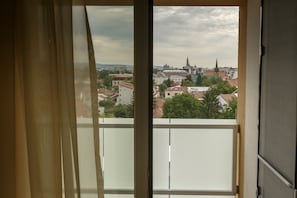 Une vue depuis un balcon, avec un paysage urbain en arrière-plan, comprenant des immeubles et le clocher d’une église.