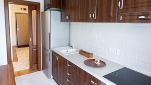 A kitchen with wooden cabinets, a stainless steel refrigerator, a white countertop, and a black induction cooktop. - Cluj Lux Apartments Platinia (Cluj-Napoca)