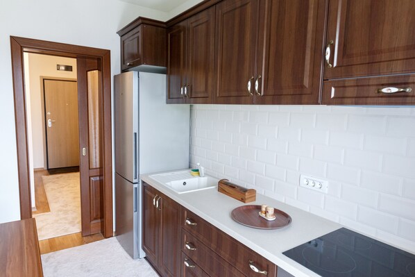 Une cuisine avec des meubles en bois, un réfrigérateur en acier inoxydable, un plan de travail blanc et une plaque de cuisson à induction noire.