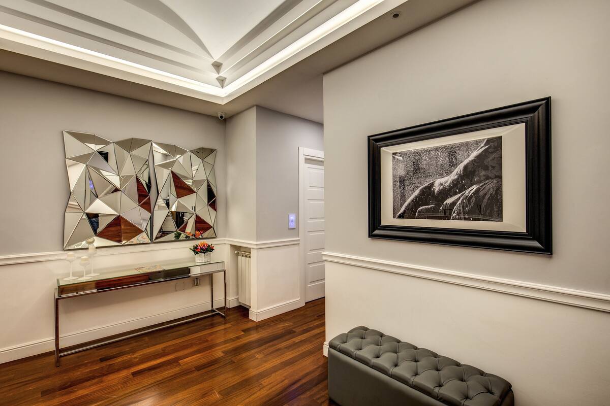 A modern interior with a wooden floor, a glass console table, a grey bench, and a framed black and white photograph on the wall.