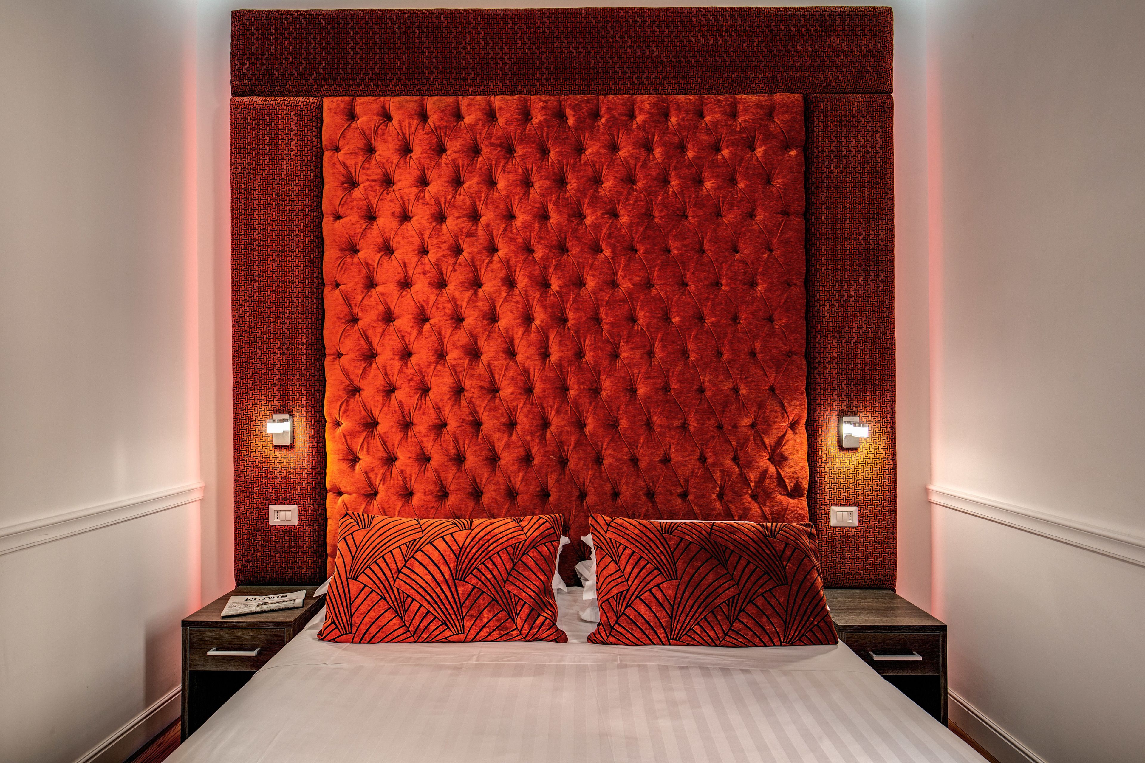 A bedroom with a tufted headboard, two bedside tables with lamps, and a bed with patterned pillows.