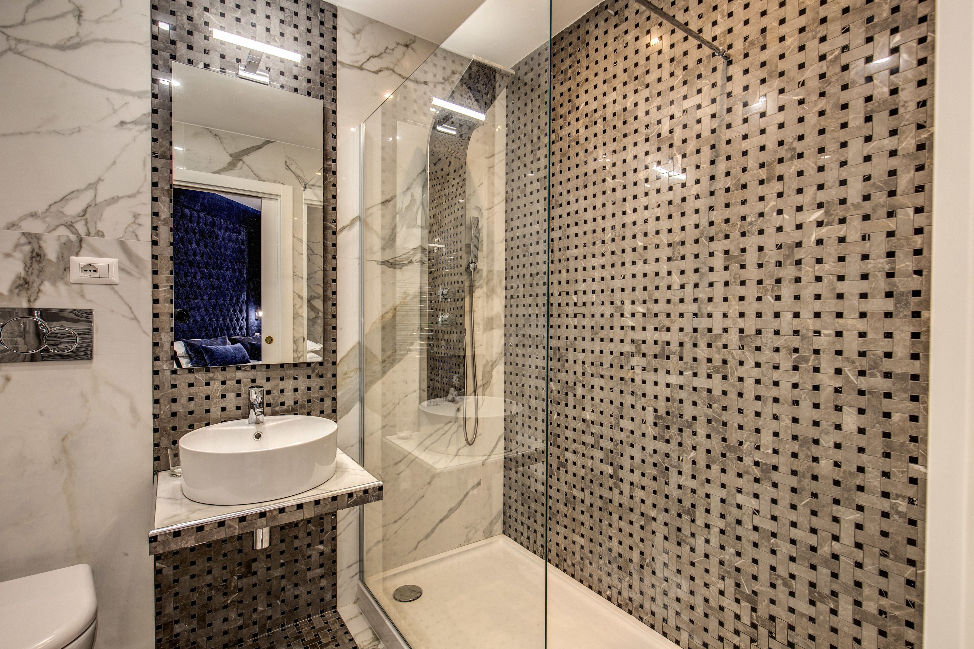 A modern bathroom with a marble sink, a glass-enclosed shower, and a patterned wall.