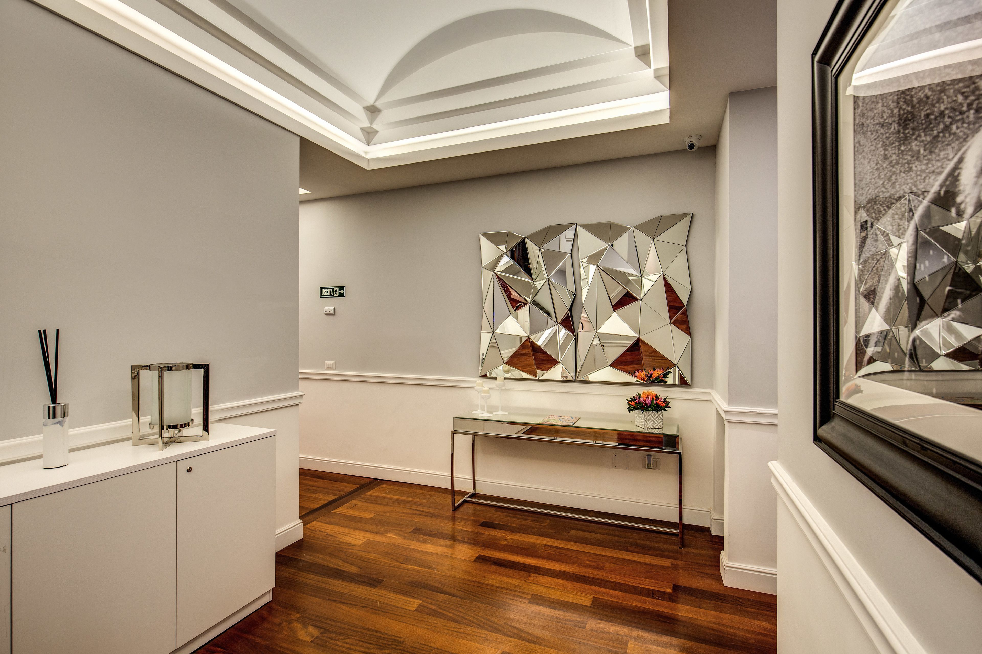 A modern hotel lobby with a wooden floor, a glass console table, and a geometric art piece on the wall.