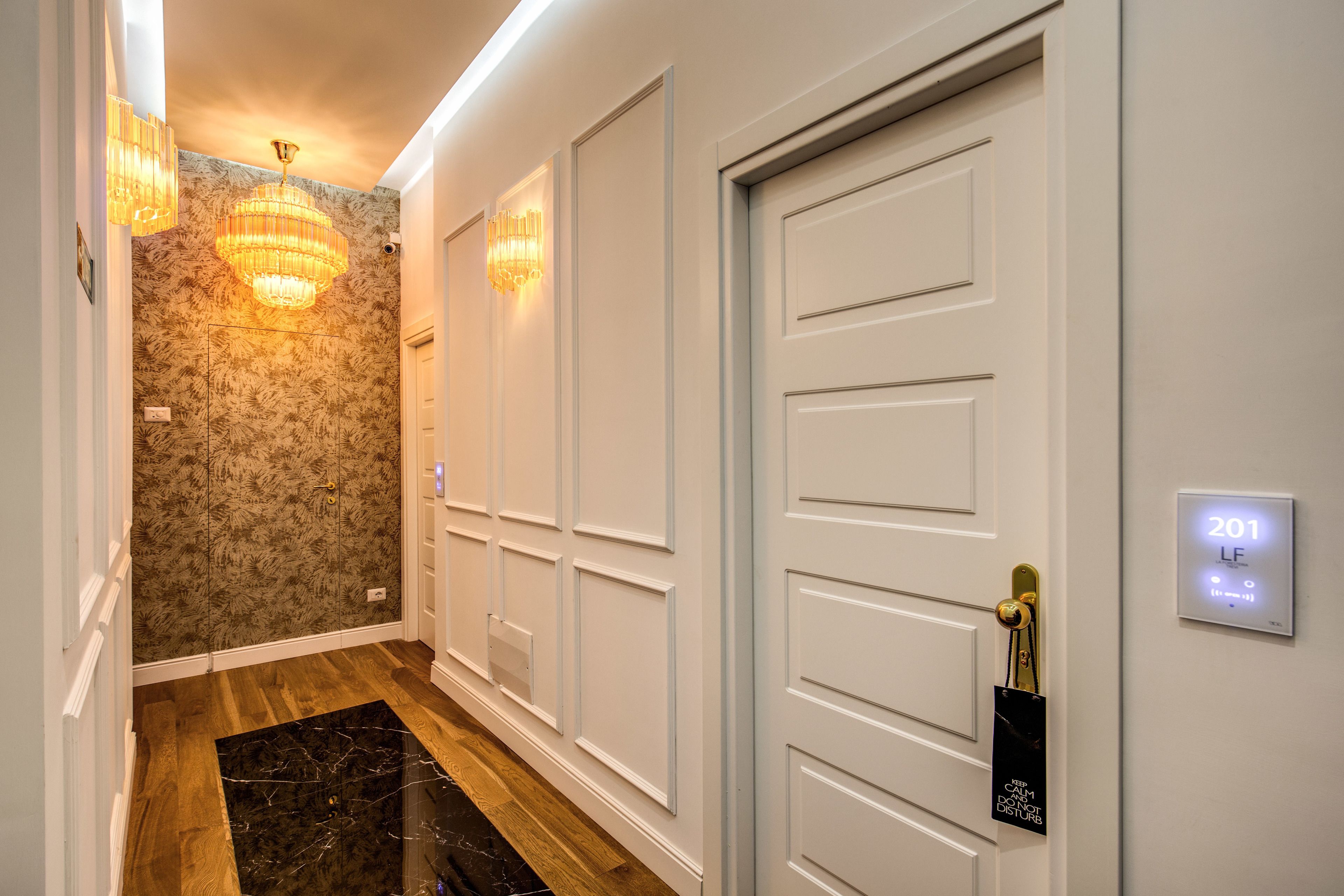 A hallway with a wooden floor, white walls, and a door with a digital lock.